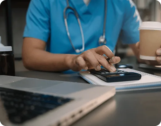 ambulance image 58785 webp Person in teal scrubs with stethoscope using a calculator beside a laptop and coffee cup