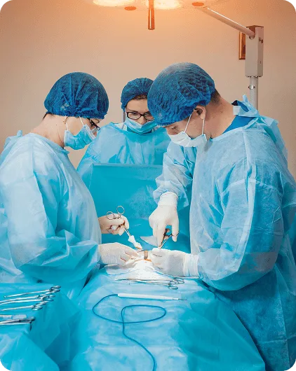 ambulatory-surgical-center image 58825 webp Surgeons in blue gowns and caps operating together beneath an overhead surgical light