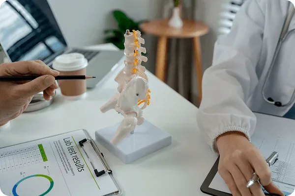 Desk with a spine model, lab test results clipboard, coffee cup, and two people's hands holding pens
