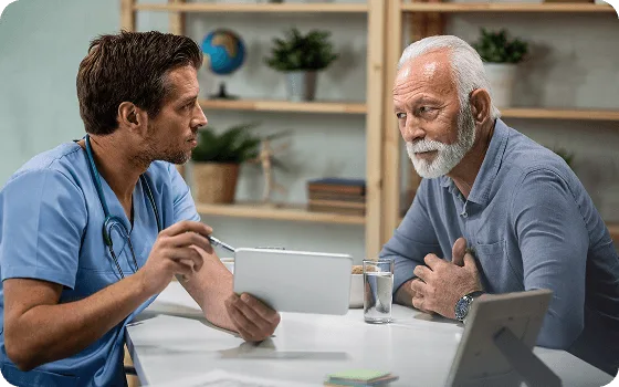 Doctor in scrubs showing a tablet to an older bearded man seated at a table