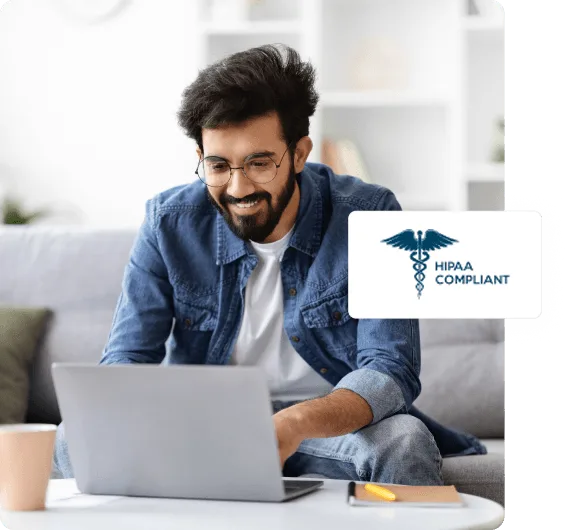 Smiling bearded man in a denim shirt working on a laptop on a sofa