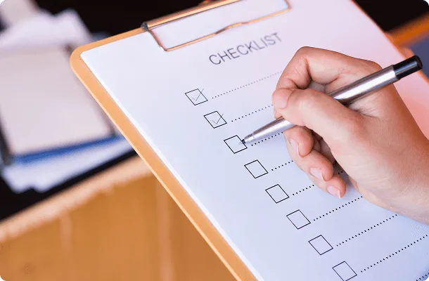 Hand ticking items on a paper checklist attached to a clipboard, with several empty boxes remaining