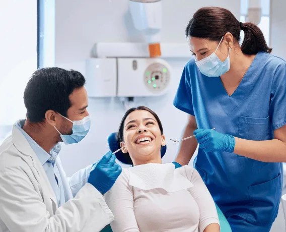 Dentist and assistant in masks and gloves treating a laughing patient in a dental chair