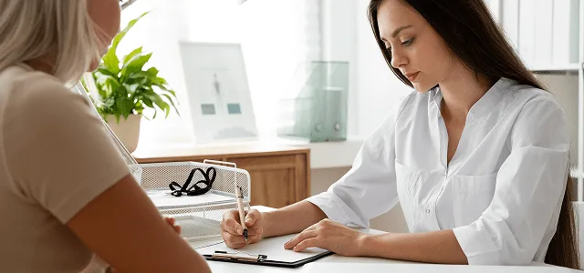 dermatology image 59937 webp Woman in white coat writing on a clipboard while sitting across from a patient