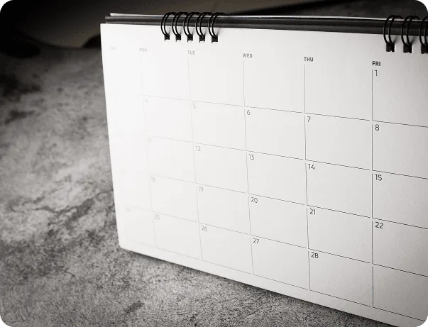 Black and white spiral-bound desk calendar standing on a textured surface with blank date boxes