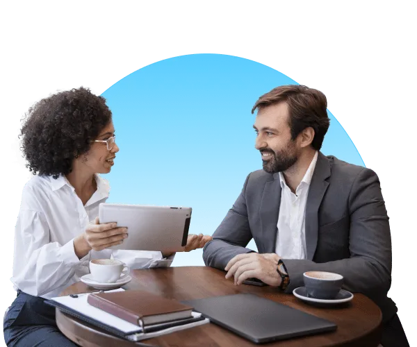 Woman holding a tablet talking with a smiling man in a blazer over coffee at a wooden table