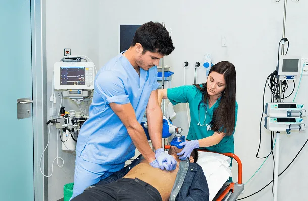 Two healthcare workers in scrubs give chest compressions and ventilation to a patient on a stretcher