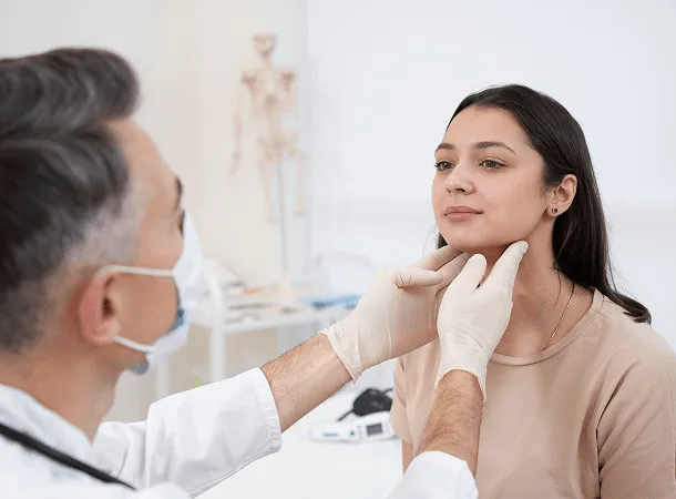 Doctor in a mask gently examining a young woman's neck with gloved hands