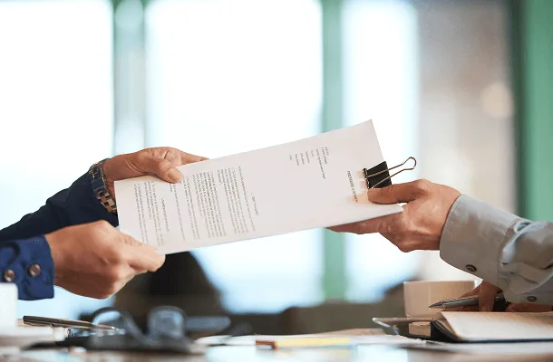 Two people exchanging a clipped paper document across a desk