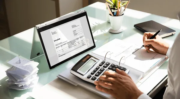 gastroenterology image 59885 webp Person using a calculator and pen at a glass desk, with a laptop showing an invoice