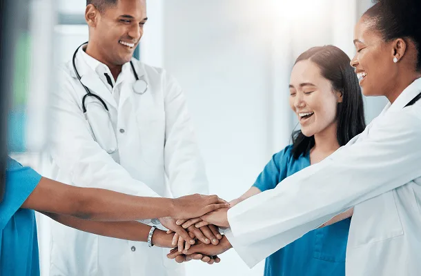 gastroenterology image 59889 webp Smiling medical staff in white coats and scrubs stacking their hands together in a huddle