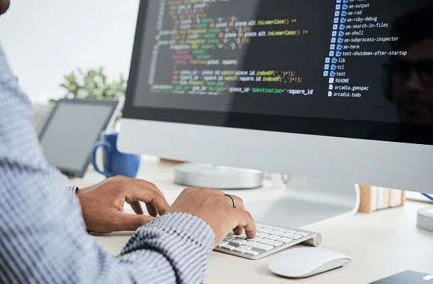 Person typing on a keyboard in front of a monitor showing lines of code