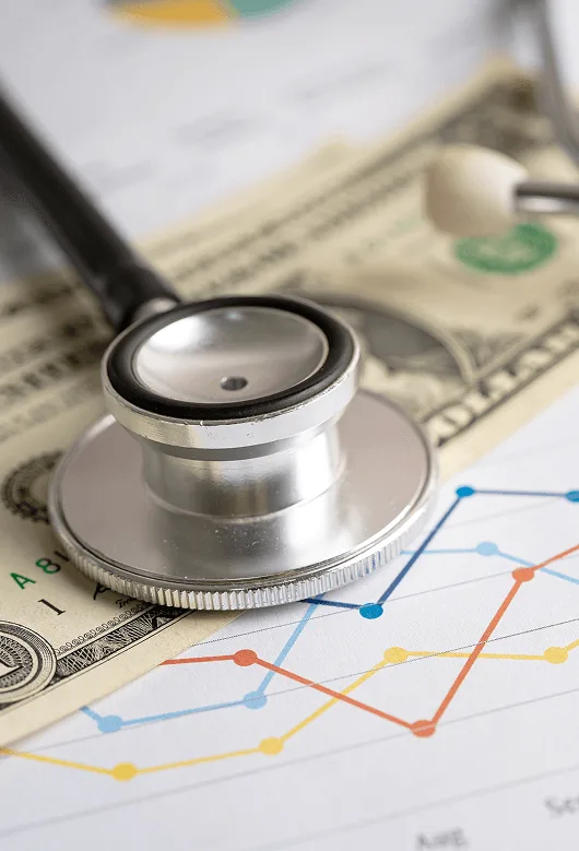 Stethoscope resting on a dollar bill and a printed line chart