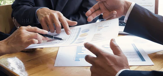 Business team members pointing at printed charts and graphs on a wooden table