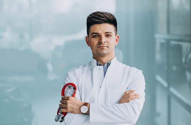 Male doctor in a white coat with arms crossed holding a red stethoscope