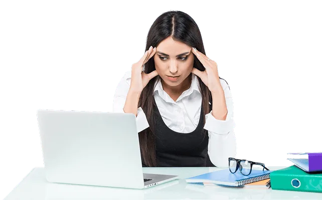 Stressed woman holding her temples while looking at a laptop, with folders and glasses on desk