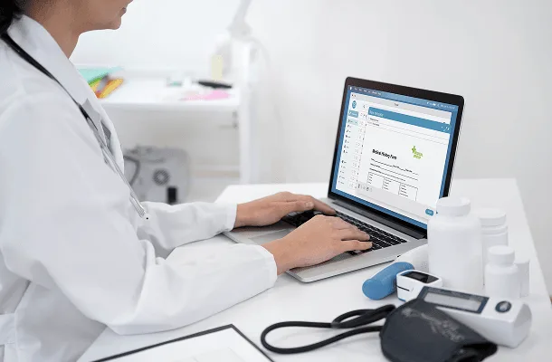 Clinician in a white coat typing on a laptop showing a medical billing form