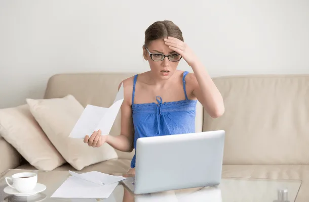 Person reviewing paperwork with concern beside a laptop
