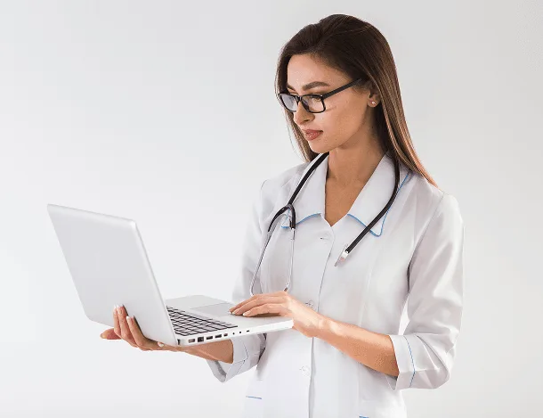 Woman in a white coat and glasses with a stethoscope looks at a laptop she holds