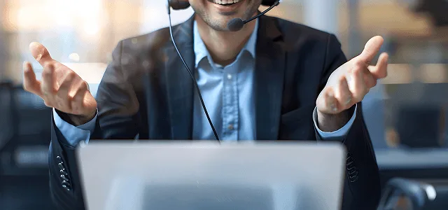 nephrology image 59702 webp Smiling customer support agent wearing a headset with open hands in front of a laptop