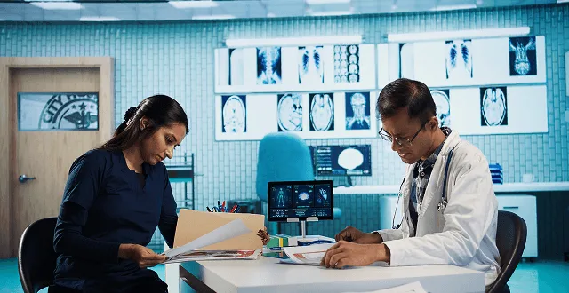 nephrology image 59706 webp Woman and doctor reviewing papers at a desk in a room with wall-mounted X-ray films