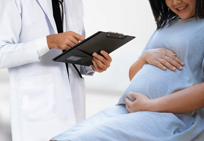 Doctor in a white coat holding a clipboard beside a smiling pregnant patient