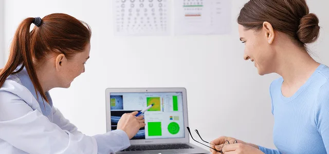 optometry image 59580 webp Eye care professional points at retinal scan results on a laptop while a patient looks on