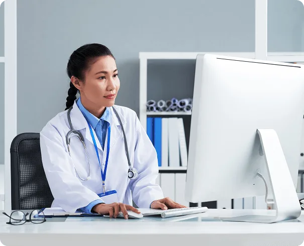 optometry image 61512 webp Clinician in white coat with stethoscope and lanyard working at a desktop computer