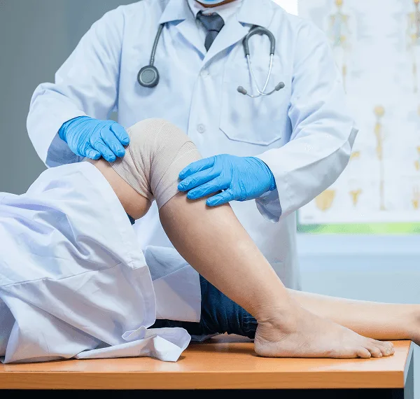 Clinician in gloves examines a patient's bandaged knee on an exam table