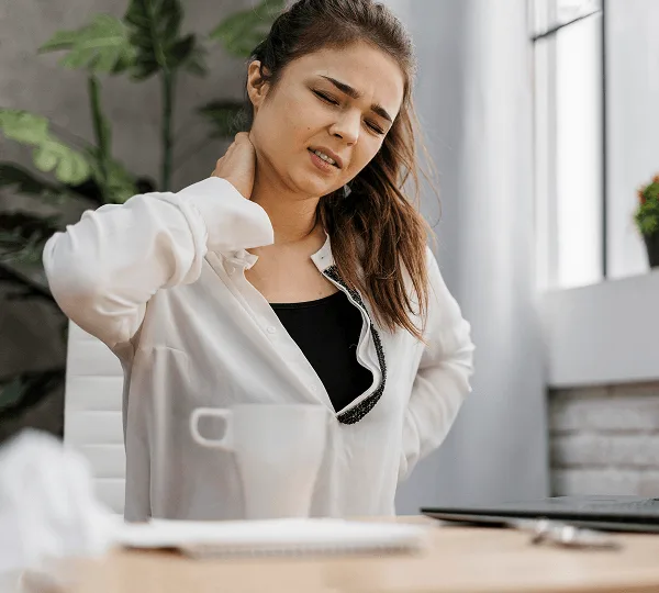 Woman at a desk grimacing with one hand on her neck and the other on her lower back