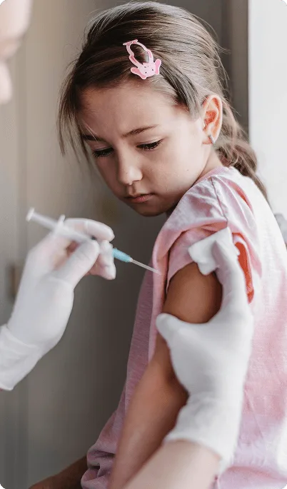 pediatric image 59490 webp Young girl looking at her upper arm as a gloved clinician prepares to give an injection