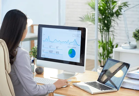 pediatric image 59493 webp Woman seated at a desk viewing a monitor with charts and graphs, with a laptop beside it