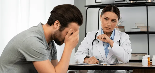 pediatric image 59495 webp Distressed man covering his face while a doctor with a stethoscope looks on across a desk