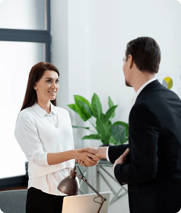Smiling woman and man in a suit shaking hands in a bright office with a plant