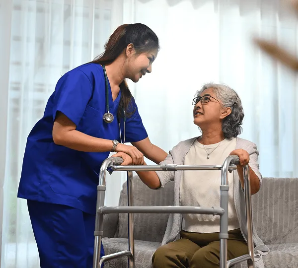 Healthcare worker in blue scrubs smiling at an older woman seated behind a walker
