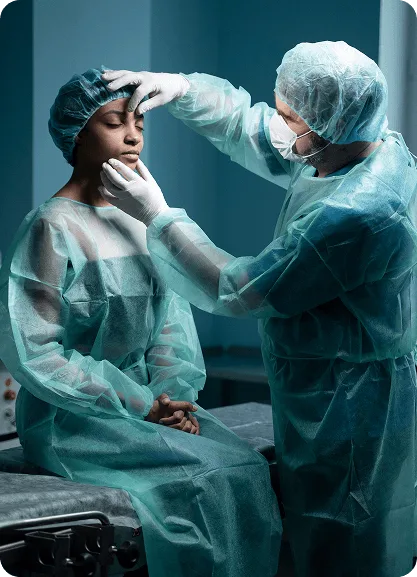 plastic-surgery image 59433 webp Surgeon in scrubs and mask touching the face of a seated patient in a surgical gown