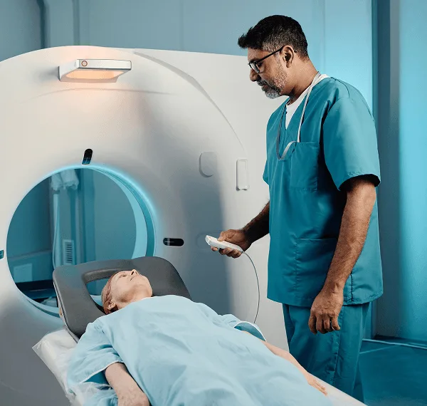 Technician in teal scrubs standing beside a patient lying in a CT scanner