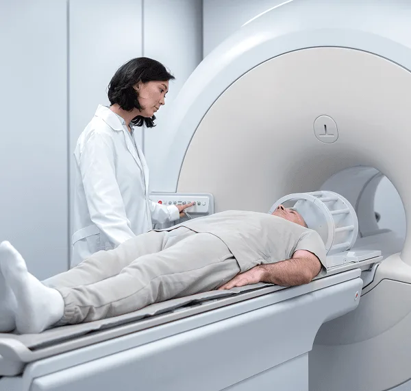 Technologist adjusts controls beside an MRI scanner while a patient lies on the table