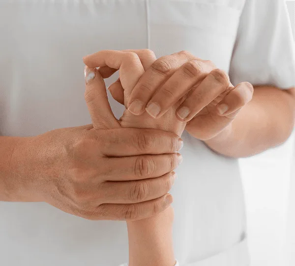 Clinician in a light tunic gently examining a patient's hand and fingers with both hands