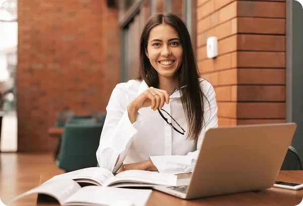 rpa-medical-billing image 62195 webp Smiling woman holding eyeglasses at a table with a laptop and open books