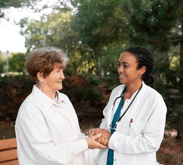 Smiling doctor in a white coat holding the hands of an older woman outdoors