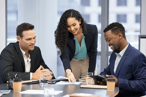 shared image 59395 webp Three colleagues in business attire smiling and reviewing papers at a conference table