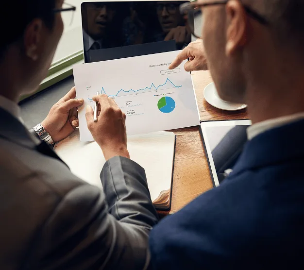 Two people in suits reviewing a printed chart with a line graph and pie chart