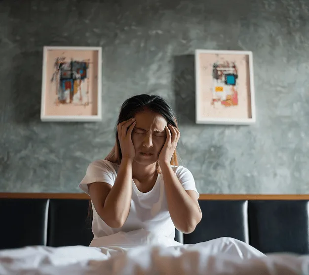 Woman sitting up in bed holding her head with both hands, looking distressed