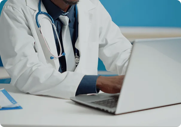 Doctor in a white coat with a stethoscope and tie typing on a laptop