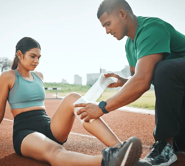 Man wrapping a bandage around a seated woman's leg on an outdoor running track