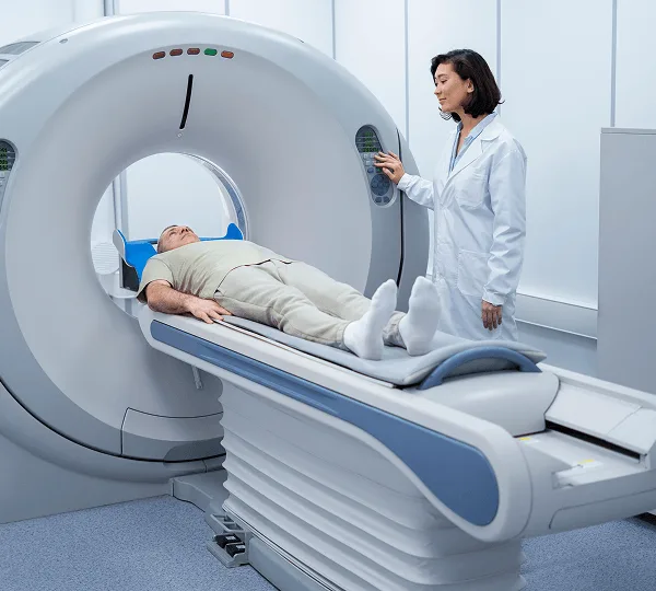teleradiology image 59237 webp Woman in a lab coat standing beside a CT scanner with a patient lying on the table