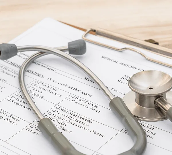 Stethoscope resting on a medical history form with checkbox lists on a clipboard