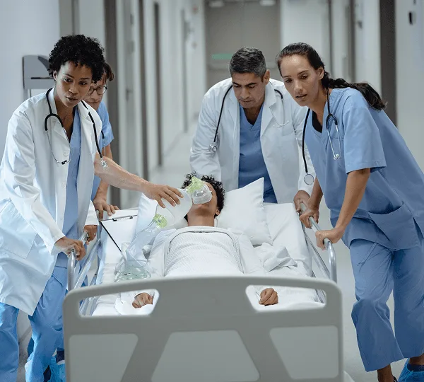 Medical staff in scrubs and white coats rushing a patient on a stretcher with an oxygen mask down a hallway