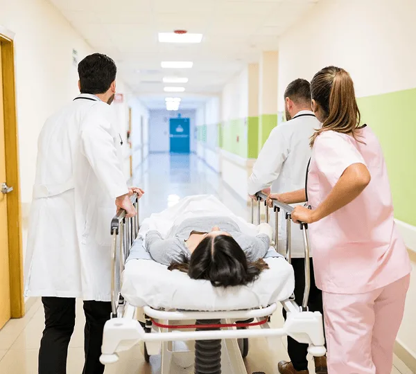 Medical staff pushing a patient on a hospital stretcher down a bright corridor